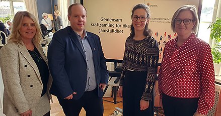 En kvinna, en man, en kvinna och en kvinna står framför en bild där det står "gemensam kraftsamling för ökad jämställdhet".