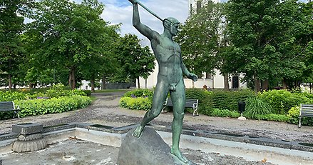 skulptur av en naken mansfigur med ett ljuster höjt i den högra handen