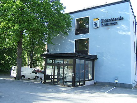 Exteriör bild på ett blått flervåningshus i betong, Stadshuset i Härnösand. Kommunvapnet sitter högst upp till höger på fasaden.