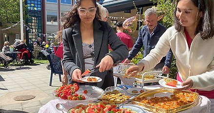 Två kvinnor står vid ett buffébord och lägger upp plockmat och bär på assietter.