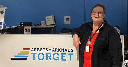 Leende kvinna framför en disk där det står "Arbetsmarknadstorget".