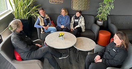 Fem kvinnor sitter samlade runt ett soffbord och samtalar.