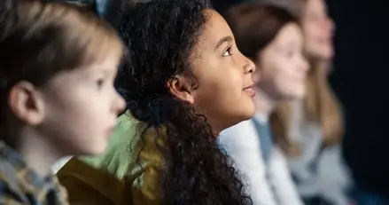 Närbild på barn i lågstadieålder som tittar på film eller teater i en släckt salong.