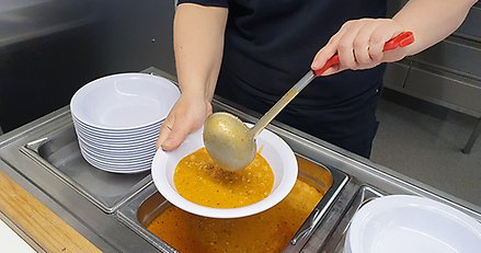 person slevar upp soppa i en tallrik med en stor slev