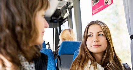 två unga kvinnor sitter på en bus och tittar på varandra