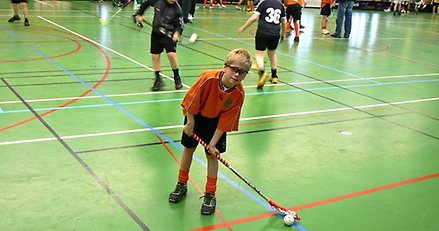 en pojke står i en idrottshall med innebandyklubba och boll 