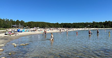 en badstrand med några människor i vattnet och många på stranden