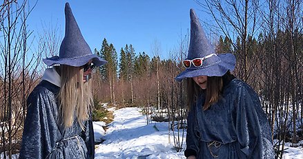 två blåklädda varelser med höga luvor på huvudet ståendes i skogen