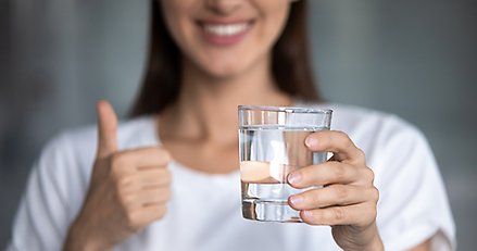 Oidentifierbar glad kvinna håller upp ett glas dricksvatten och gör tummen upp.