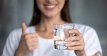 Oidentifierbar glad kvinna håller upp ett glas dricksvatten och gör tummen upp.