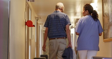 En äldre man och en kvinna går i en korridor. 