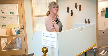 Kvinna står bakom skärm vid ett ställ med valsedlar