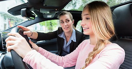Kvinnlig trafiklärare som utbildar en ung tjej i en bil.