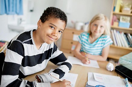 Pojke och flicka sitter vid ett bord i skolmiljö och skriver.