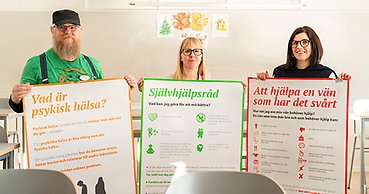 Tre kuratorer som står och håller upp stora färgglada affischer som ger råd om psykisk hälsa