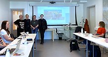 Mötesdeltagare runt ett hästskoformat bord, tittar mot fyra personer vid en whiteboard. 
