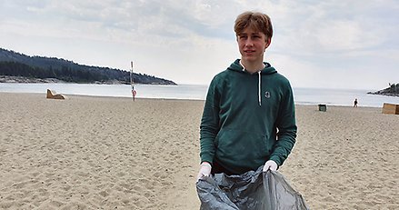En kille står med en sopsäck på en strand. 