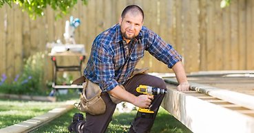 en snickare står på knä vid en altan med en skruvdragare i handen