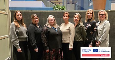 Gruppbild med sju kvinnor som är uppställda för fotografering inomhus.