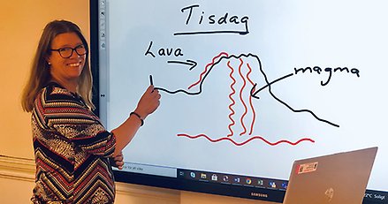 Läraren jenny framför en smartboard med en penna i handen. På tavlan, en skiss av en vulkan.